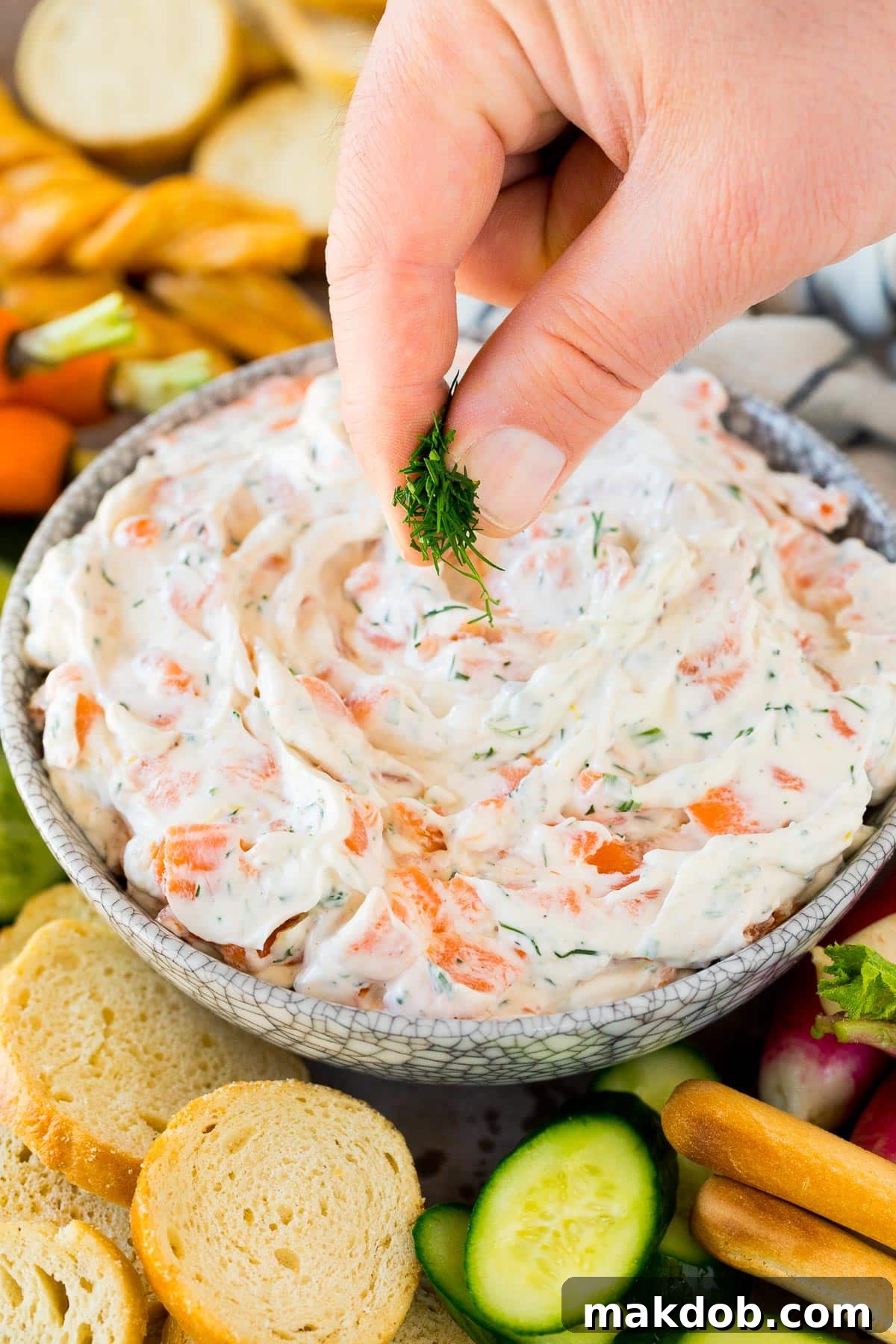 Decadent Smoked Salmon Dip 5 A hand delicately garnishing the creamy smoked salmon dip with fresh green dill, adding a final touch of freshness and visual appeal to the appetizer.