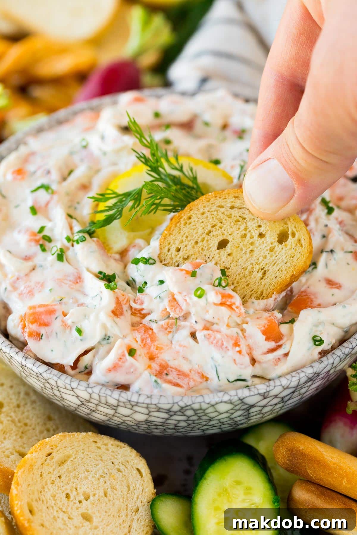 Decadent Smoked Salmon Dip 6 A hand delicately scooping a generous portion of creamy smoked salmon dip onto a golden-brown crostini, showcasing the perfect texture and inviting presentation of the appetizer.