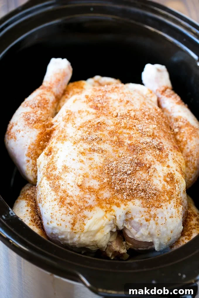 Slow Cooker Whole Chicken | Slow Cooker Rotisserie Chicken | Crock Pot Roasted Chicken | Crock Pot Whole Chicken #chicken #slowcooker #crockpot #glutenfree #dinner #dinneratthezoo A raw whole chicken seasoned with spices, placed on a foil ring inside a slow cooker, ready for cooking.