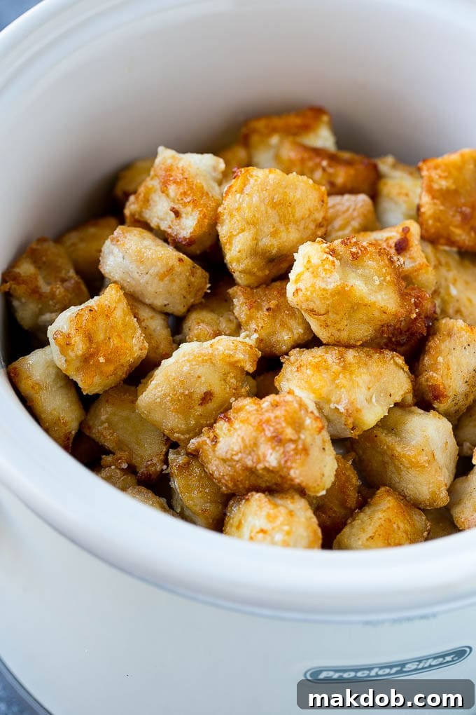 Diced, cornstarch-coated chicken pieces browning in a large skillet over medium-high heat, before being added to a slow cooker for orange chicken.