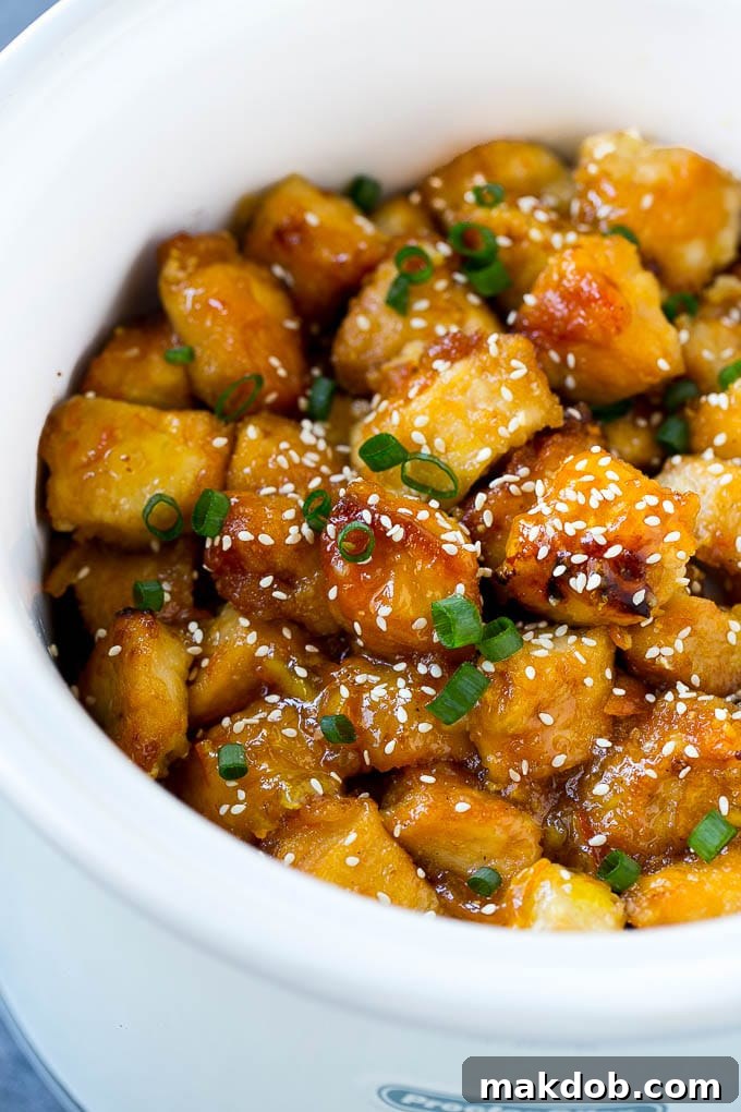 Finished Slow Cooker Orange Chicken in a Crock-Pot, beautifully garnished with fresh green onions and toasted sesame seeds, ready to be served hot.