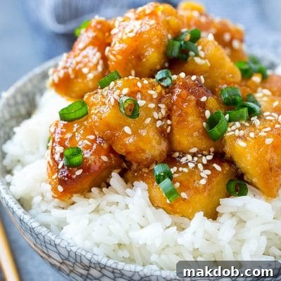 Slow cooker orange chicken served over a bowl of rice, garnished with green onions and sesame seeds.