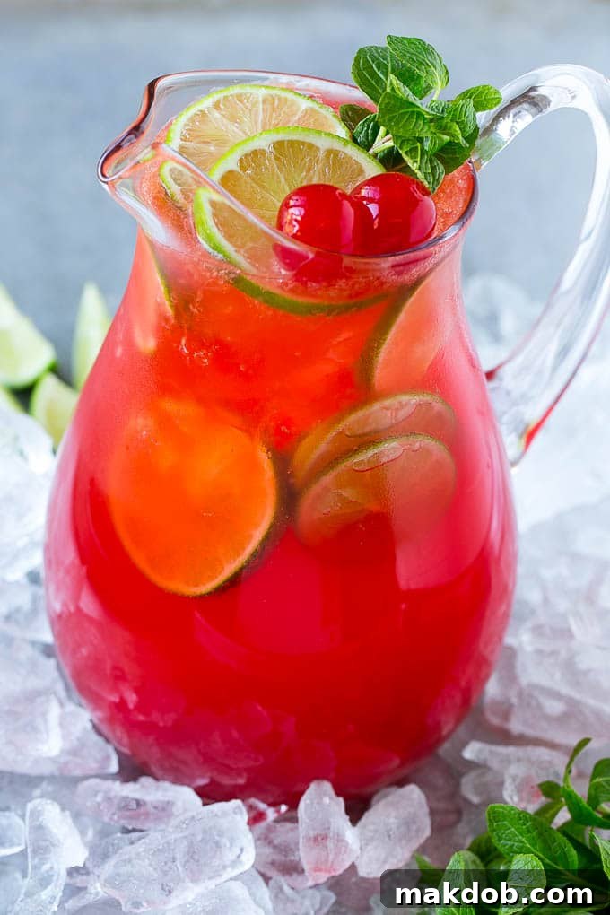 Cherry Limeade Recipe | Sonic Cherry Limeade | Limeade Recipe #limeade #drink #cherry #lime #dinneratthezoo A glass pitcher of cherry limeade garnished with slices of fresh lime and maraschino cherries.