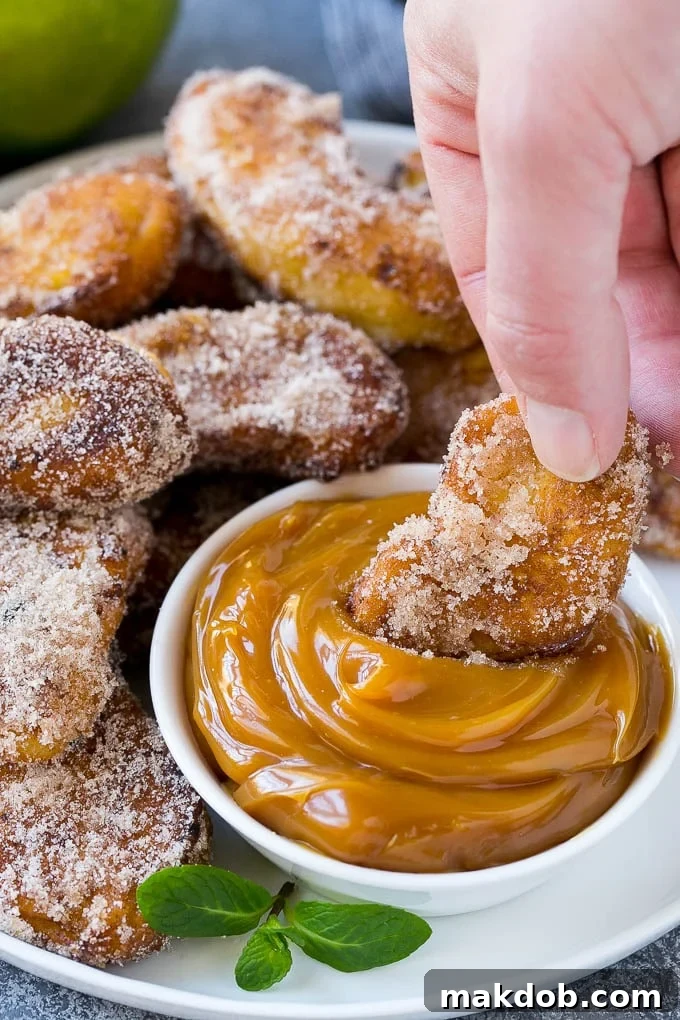 A crispy apple fry being dipped into a rich, golden caramel sauce, highlighting the perfect pairing.