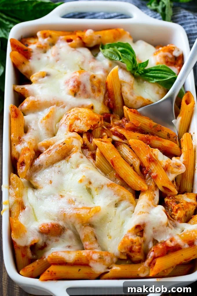 Chicken parmesan pasta in a baking dish topped with melted cheese and garnished with fresh basil.