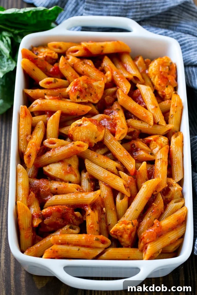 A pan of penne pasta and cooked chicken in marinara sauce.