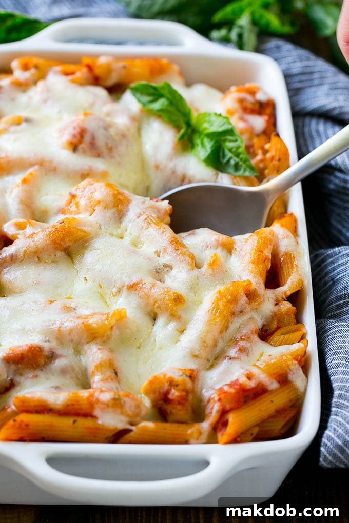 A baking dish of penne pasta with chicken, parmesan cheese and mozzarella cheese.