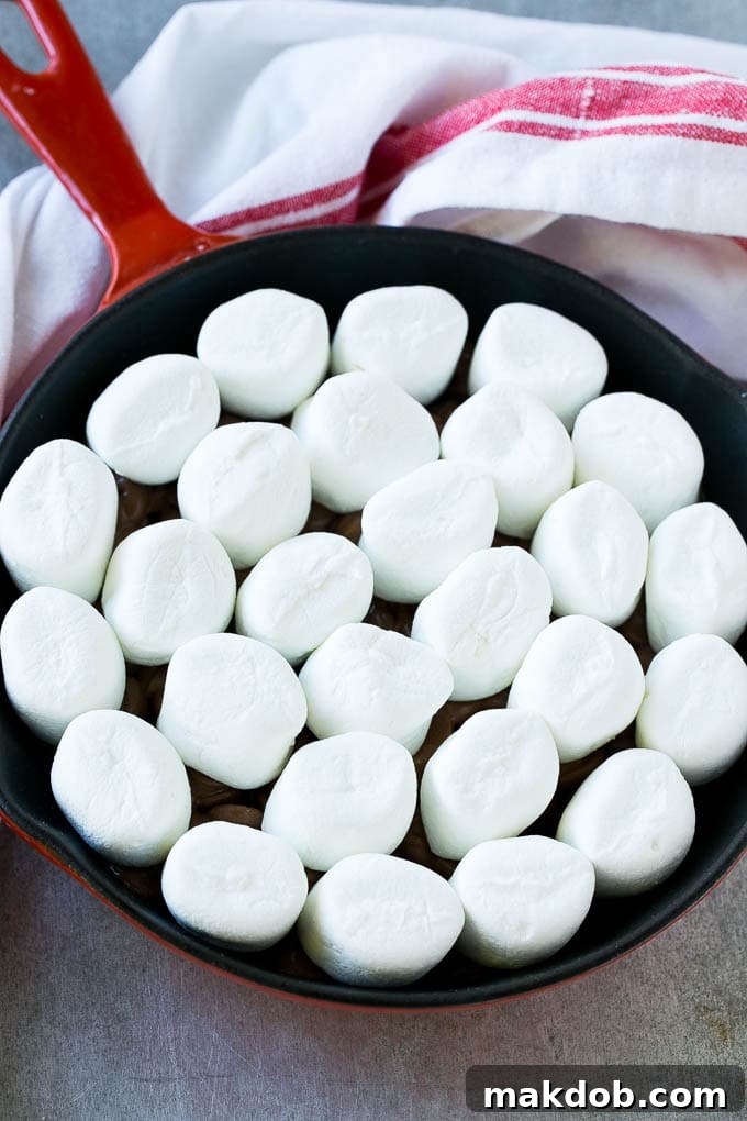 A pan of chocolate chips topped with whole marshmallows, ready for the oven.