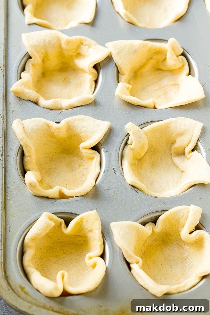 Crescent roll dough carefully pressed into the individual wells of a muffin tin, forming perfect little crust cups.