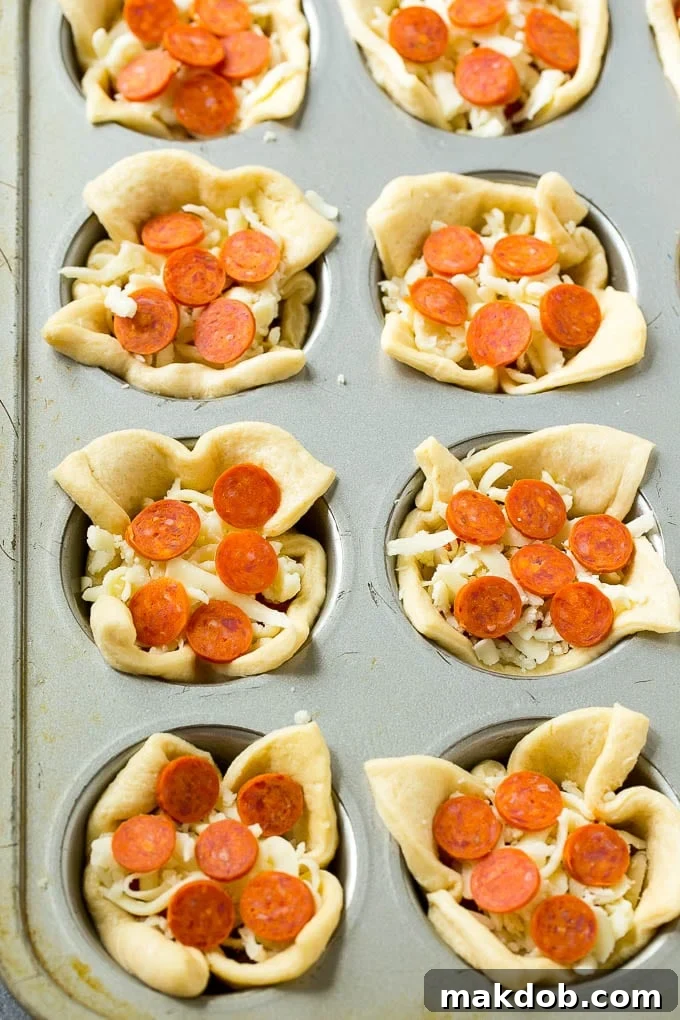 Unbaked crescent roll dough cups, perfectly formed and filled with rich pizza sauce, shredded cheese, and mini pepperoni, ready for the oven.