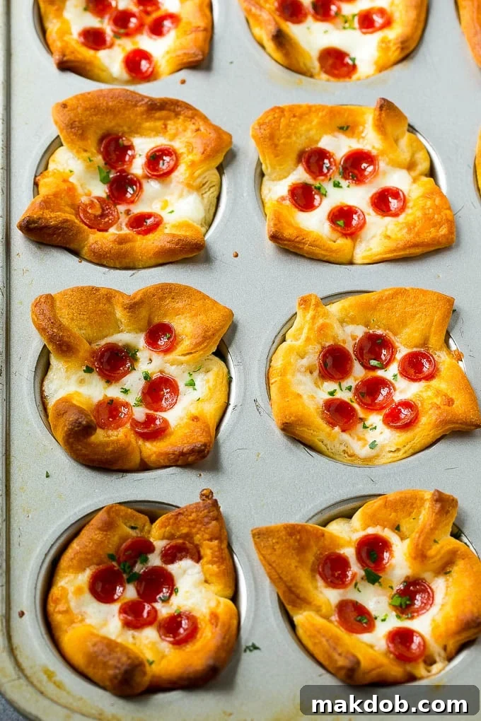 A muffin tin filled with freshly baked, golden-brown savory pizza muffins, featuring melted cheese and visible pepperoni, ready to be enjoyed.
