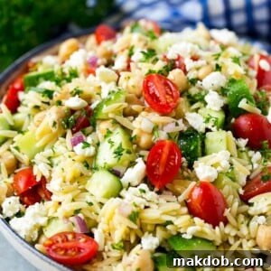 Orzo salad presented in a charming serving bowl, adorned with fresh tomatoes, crisp cucumbers, and wholesome chickpeas.