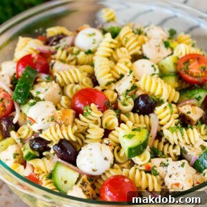 A generous bowl of chicken pasta salad brimming with grilled chicken pieces, ripe tomatoes, crisp cucumbers, and cheese, ready to serve.