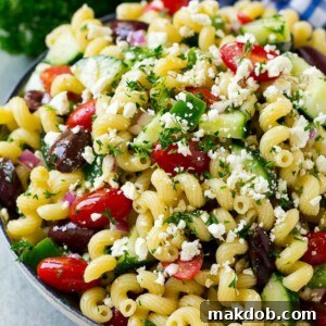 Greek pasta salad in a serving bowl, vibrantly garnished with fresh parsley, highlighting the colorful ingredients.