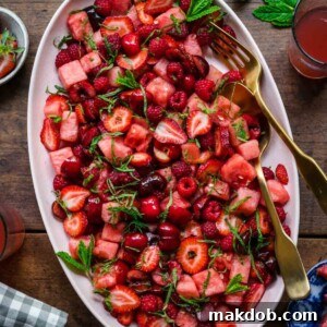 A refreshing Watermelon Fruit Salad with Berries and Lime Dressing, presented in a large oval bowl filled with cherries, strawberries, and juicy watermelon.