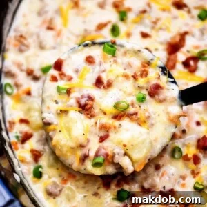 A bubbling pot of slow cooker bacon cheeseburger soup, with a ladle ready to serve a hearty portion.