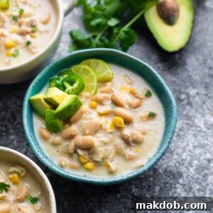 A inviting bowl of creamy white chicken chili, elegantly garnished with fresh avocado pieces on top.