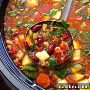 A ladle full of vibrant slow cooker minestrone soup, brimming with fresh vegetables and pasta.