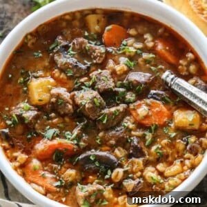 A hearty bowl of slow cooker beef and barley stew, garnished with carrots and fresh herbs.