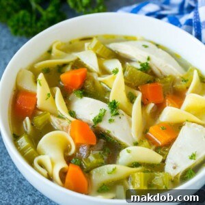 A bowl of classic crock pot chicken noodle soup with tender carrots and garnished with fresh parsley.