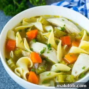 A warm bowl of crock pot chicken noodle soup, garnished with fresh parsley and showcasing tender chicken, bright carrots, and comforting egg noodles.
