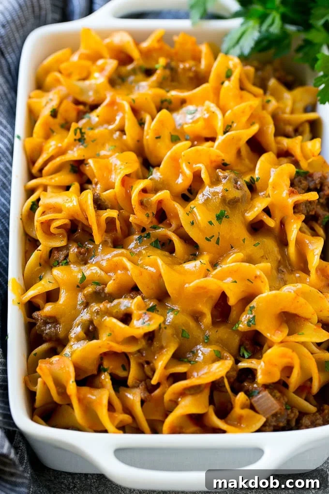 Beef noodle casserole in a serving dish topped with melted cheddar cheese and parsley.