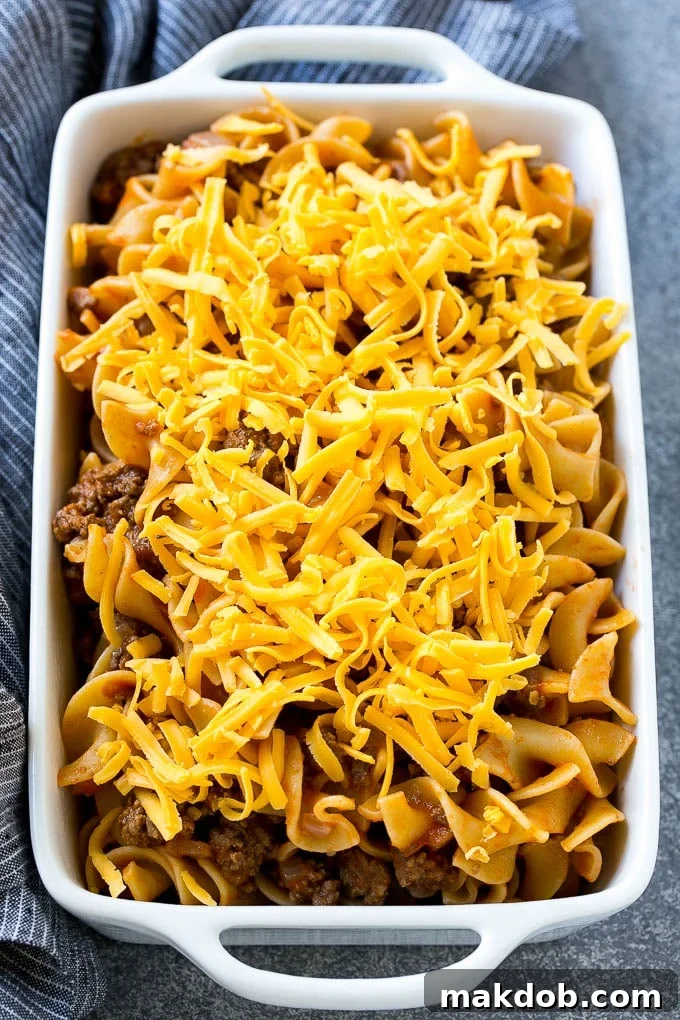A pan of ground beef and egg noodles in tomato sauce, topped with shredded cheddar cheese.