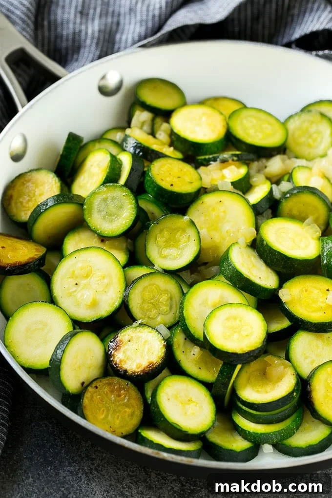 Zucchini Gratin Recipe | Cheesy Zucchini | Baked Zucchini | Easy Zucchini Recipe #zucchini #casserole #cheese #dinner #sidedish #dinneratthezoo Sliced zucchini and diced onions being sauteed in a skillet, creating a fragrant base for the gratin.