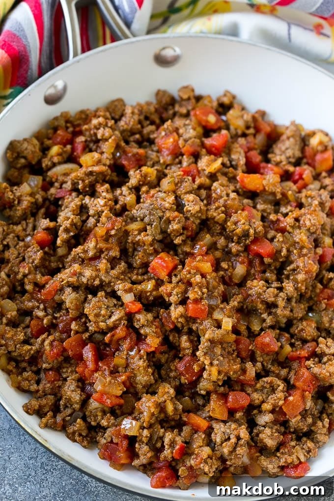 A skillet full of perfectly seasoned ground beef, onions, and diced tomatoes for tacos.