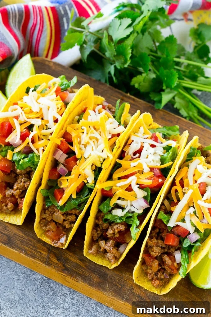 Crispy ground beef tacos with a variety of toppings including shredded lettuce, diced tomato, and melted shredded cheese.
