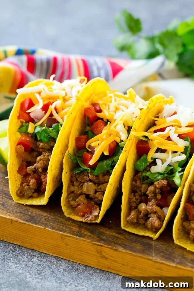 Hard taco shells generously filled with seasoned ground beef, vibrant shredded lettuce, fresh diced tomatoes, minced onions, and a sprinkle of shredded cheese.
