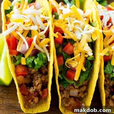 Ground beef tacos in hard taco shells topped with shredded cheese, lettuce, tomato and onion.