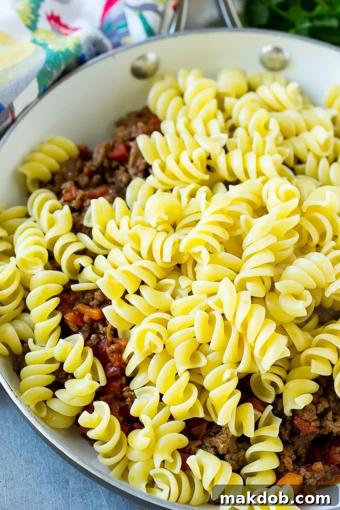 A skillet of cooked ground beef seasoned with tomatoes, and rotini pasta.
