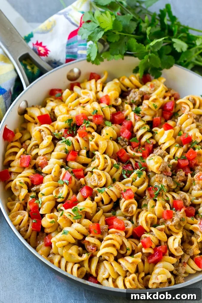 A skillet of taco pasta topped with fresh diced tomatoes and cilantro.