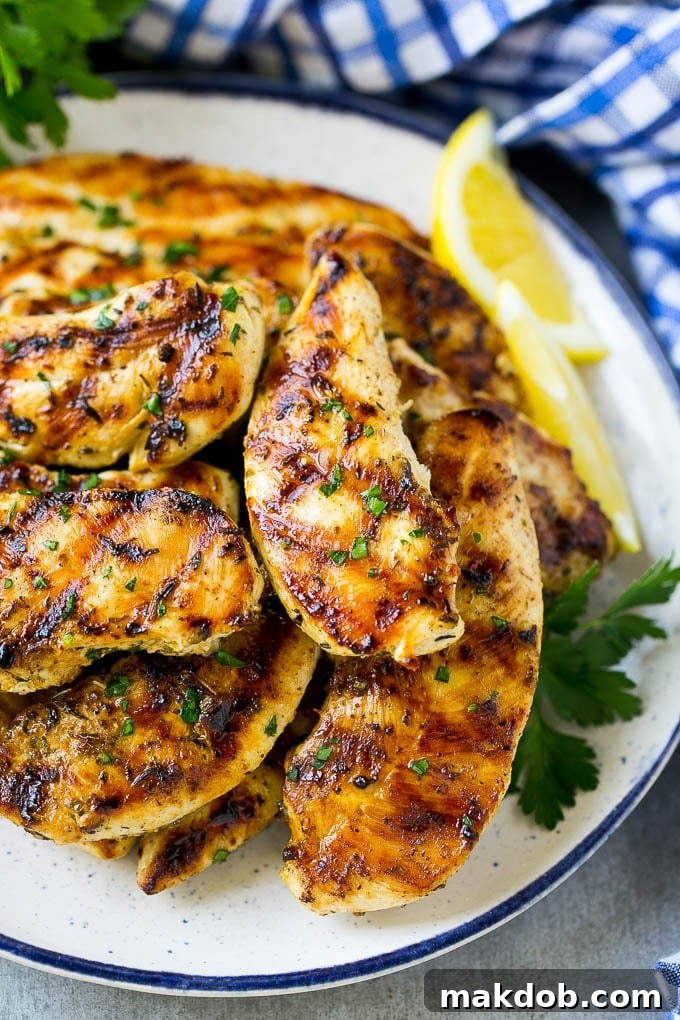 A pile of grilled chicken tenders topped with fresh herbs and garnished with lemon wedges.