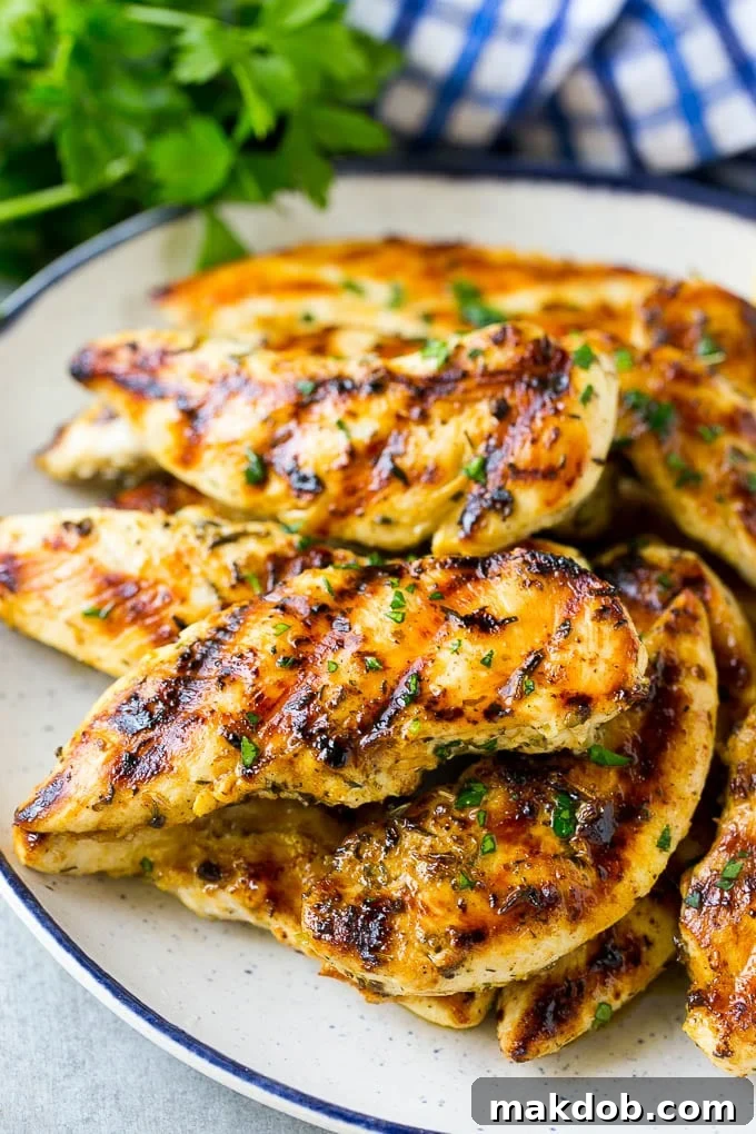 A plate of grilled chicken tenders topped with chopped parsley.