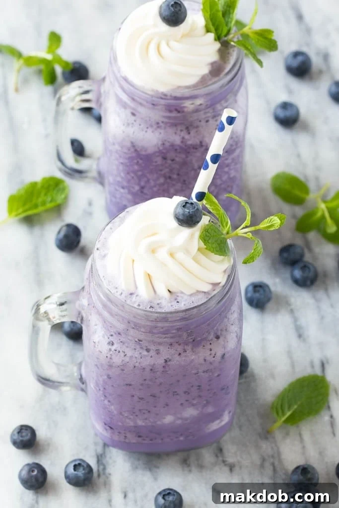 Close-up of a refreshing blueberry milkshake with whipped cream and fresh mint.