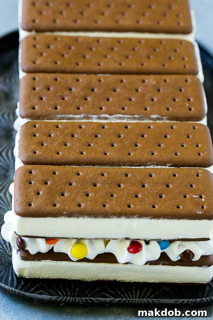 Layers of an ice cream sandwich cake showcasing whipped topping and chocolate candy between each sandwich layer.