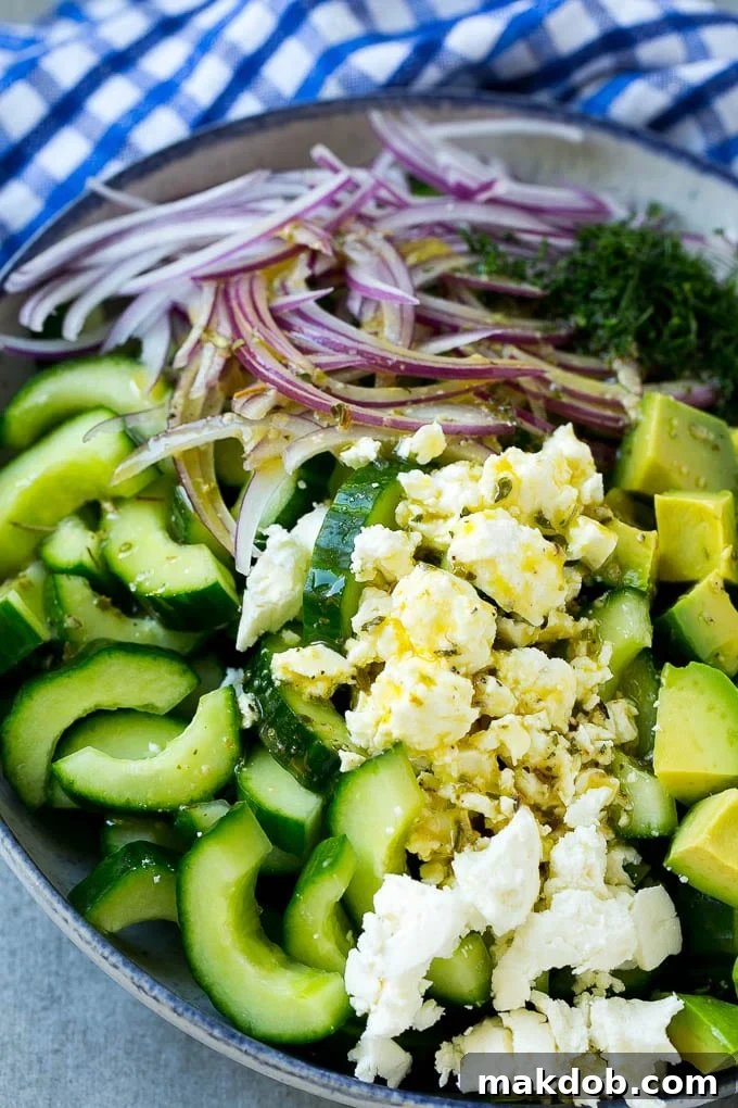 A close-up view of the cucumber feta salad, showcasing the freshly chopped vegetables and crumbled feta cheese, generously topped with the zesty Greek dressing and ready to be tossed.