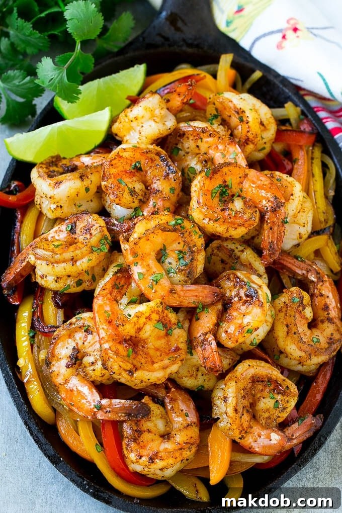A vibrant skillet of perfectly cooked shrimp fajitas, adorned with colorful peppers, onions, fresh cilantro, and bright lime wedges.