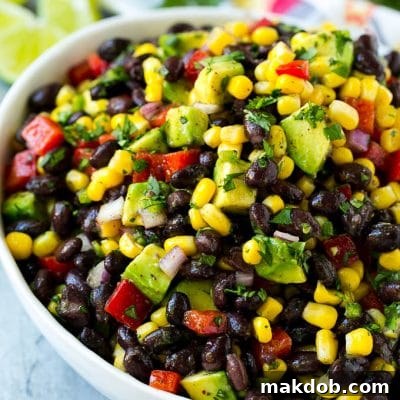 A bowl of black bean and corn salad loaded with avocado and red pepper, garnished with fresh cilantro.