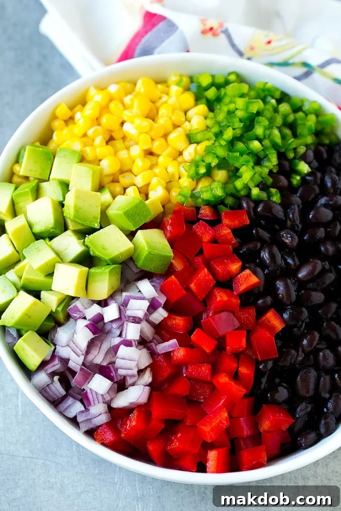 Fresh Black Bean and Corn Salad Ingredients A bowl filled with individual ingredients for black bean and corn salad: black beans, corn, diced red peppers, minced jalapeno, red onion, and avocado.