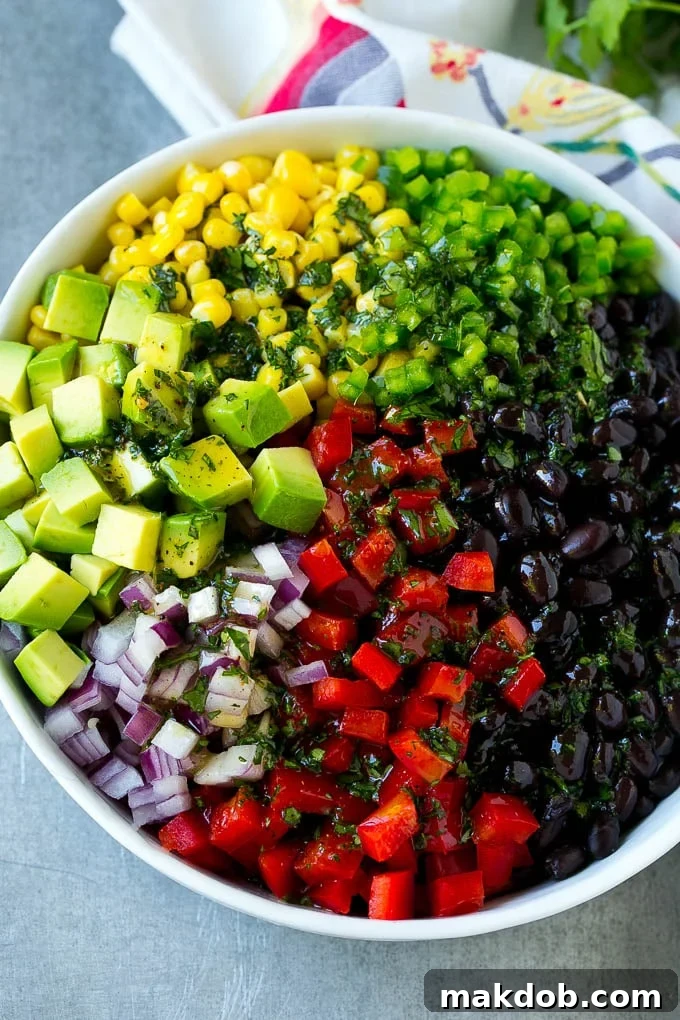 Mixing Black Bean and Corn Salad with Dressing Black beans, corn, and assorted fresh vegetables being topped with zesty cilantro lime dressing in a bowl.