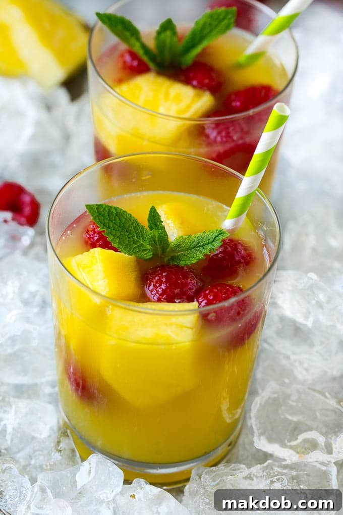 Glasses of pineapple punch with fresh pineapple and raspberries.