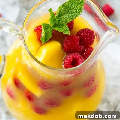 A pitcher of pineapple punch with fresh pineapple, raspberries and mint.