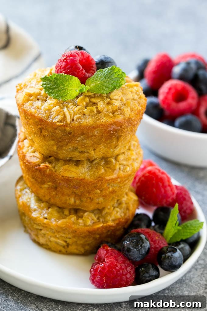 A stack of baked oatmeal cups topped with syrup, raspberries, blueberries and mint.