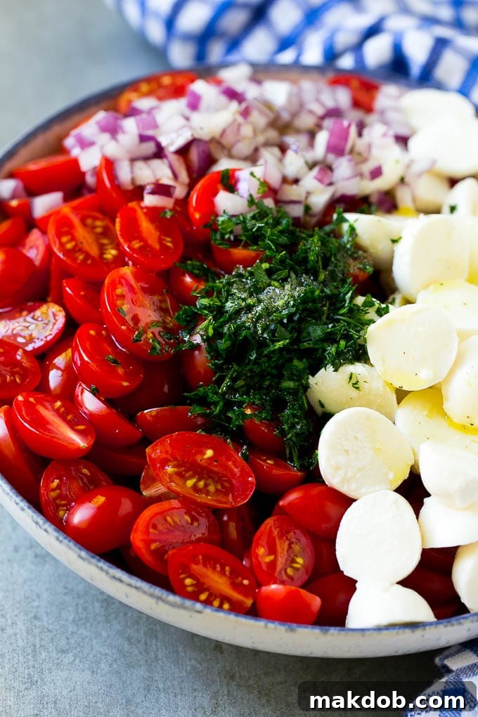 Cherry tomatoes, herbs, mozzarella balls and red onion drizzled with dressing in a bowl.
