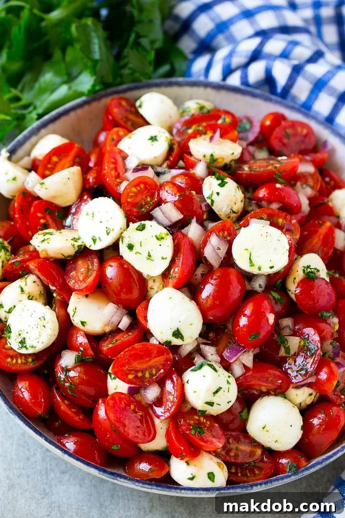 A serving bowl of tomato mozzarella salad with cherry tomatoes, herbs and red onion.