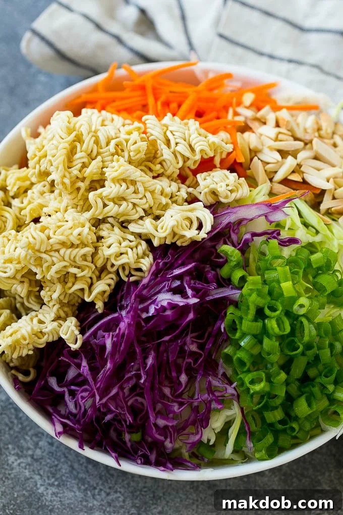 Shredded cabbage, broken up ramen noodles, shredded carrots, almonds and green onions in a bowl.