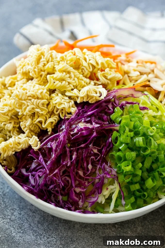 Cabbage, ramen noodles, green onions and carrots in a bowl, drizzled with dressing.